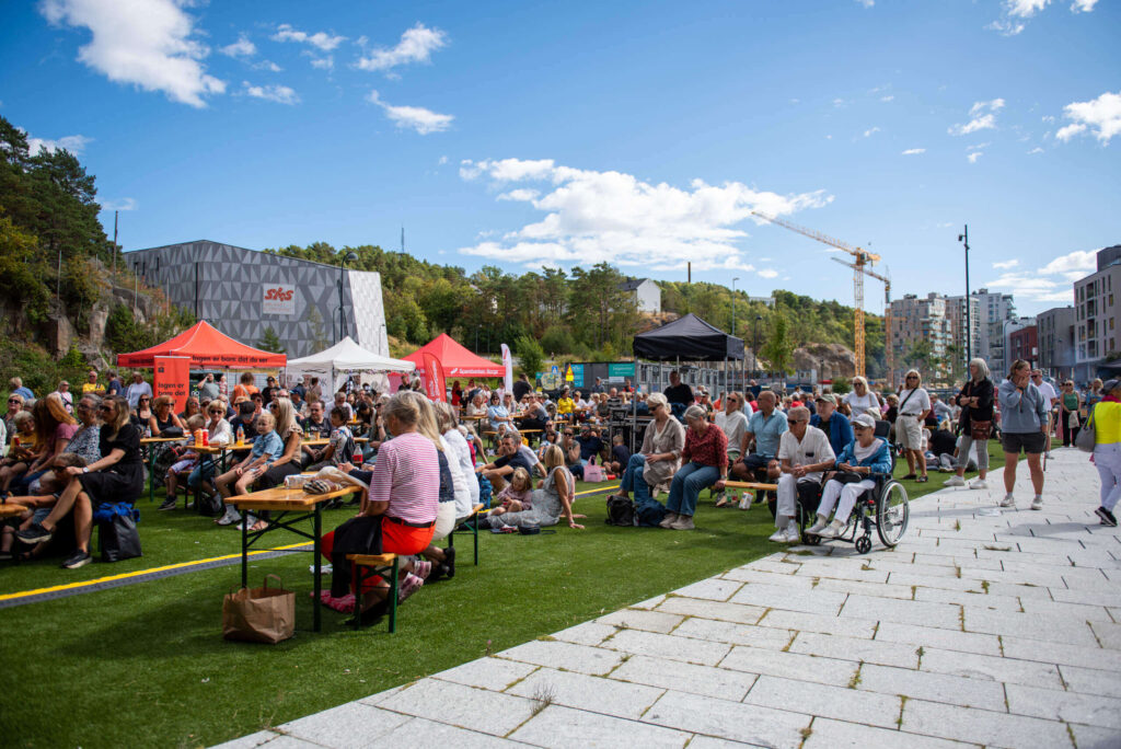 Folkemengde koser seg på gresset foran scenen under Kanalbyenfestivalen 2026